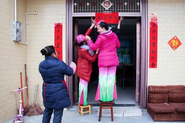 Z17443-7-277263-153****4267-文化惠民过大年（组照-4）文艺志愿者演员在演出前送春联到农家，帮助村民张贴春联。2016年1月摄于四川芦山县思经乡。