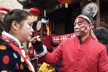 男的在自己的脸上画了一条吉祥飞龙，此时正在为姑娘画凤，龙凤吉祥，年年风调雨顺年年丰收。