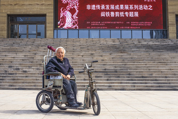 《像鹰一样飞翔-记残疾剪纸艺术家阎铁鲁》在其作品展馆前.